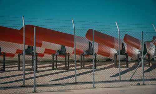 A metal fence with barb wire and metal canoes behind it with blue sky in the background